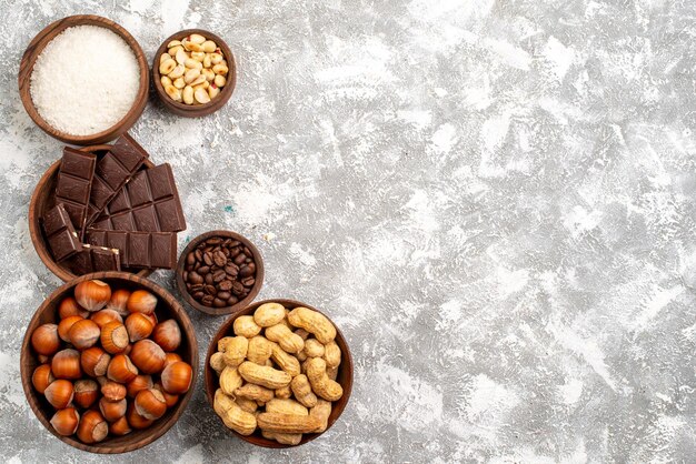 Vista dall'alto di barrette di cioccolato con nocciole e arachidi sulla superficie bianca