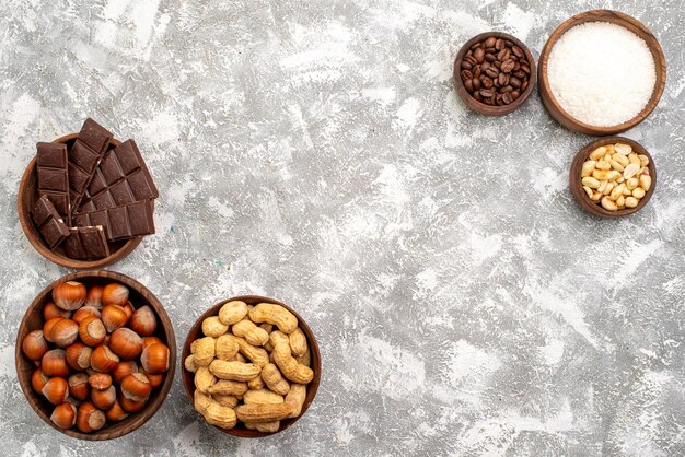 Vista dall'alto di barrette di cioccolato con nocciole e arachidi sulla superficie bianca
