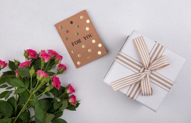 Vista dall'alto di bellissime rose rosa con foglie e confezione regalo bianca su sfondo bianco