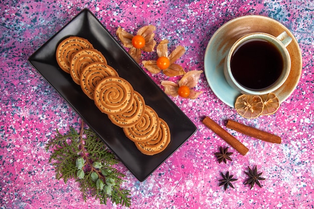 Vista dall'alto di biscotti dolci con cannella e tazza di tè sulla superficie rosa chiaro