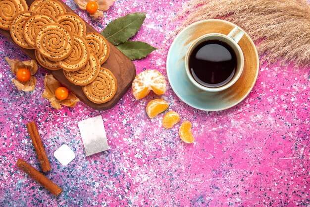 Vista dall'alto di biscotti dolci rotondi con una tazza di tè e mandarini sulla superficie rosa