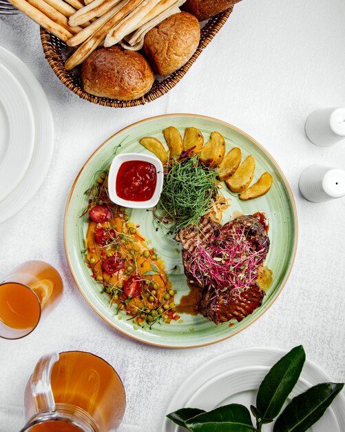 Vista dall'alto di bistecche di manzo servita con patatine fritte, insalata e ketchup