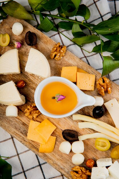 Vista dall'alto di burro fuso con diversi tipi di pezzi di uva formaggio olive noci sul tagliere sul plaid decorato con foglie