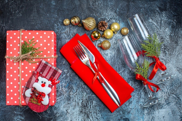 Vista dall'alto di calici di vetro caduti e set di posate accessori per la decorazione confezione regalo e calzino natalizio su sfondo scuro