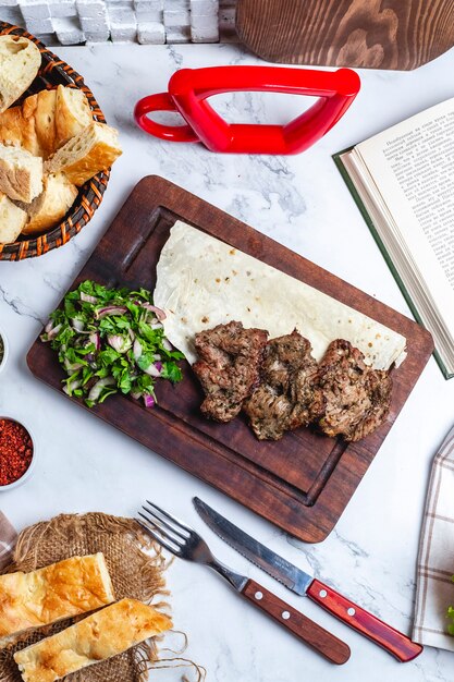 Vista dall'alto di carne di kebab con spezie ed erbe su lavash su una tavola di legno