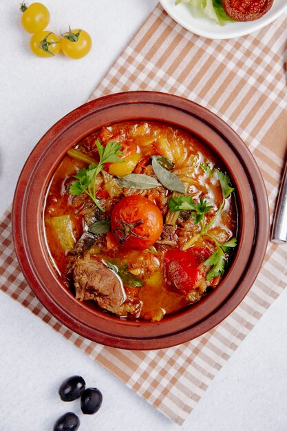 Vista dall'alto di carne in umido con patate e pomodori in una pentola di terracotta