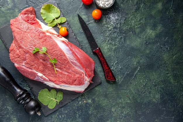 Vista dall'alto di carne rossa fresca cruda e verdure su tagliere coltello pomodori martello di legno su sfondo nero verde colori misti