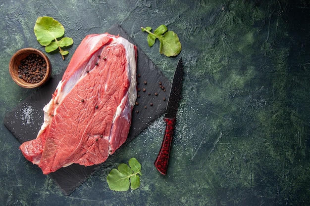 Vista dall'alto di carne rossa fresca cruda su tagliere pepe e coltello su sfondo nero verde mix di colori