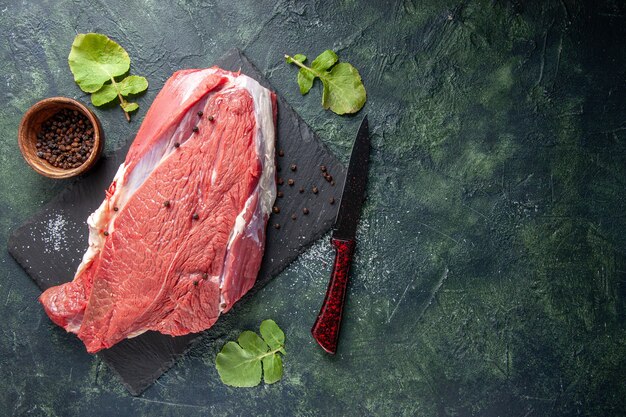 Vista dall'alto di carne rossa fresca cruda su tagliere pepe e coltello su sfondo nero verde mix di colori