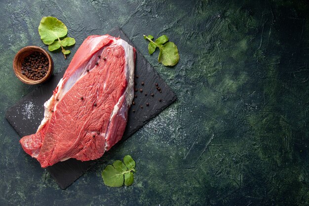 Vista dall'alto di carne rossa fresca cruda su tagliere pepe su sfondo nero verde colori mix