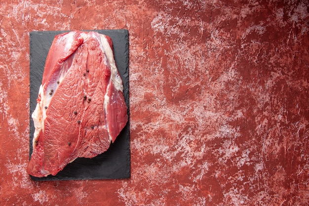 Vista dall'alto di carne rossa fresca cruda su tavola nera sul lato destro su sfondo rosso pastello ad olio con spazio libero