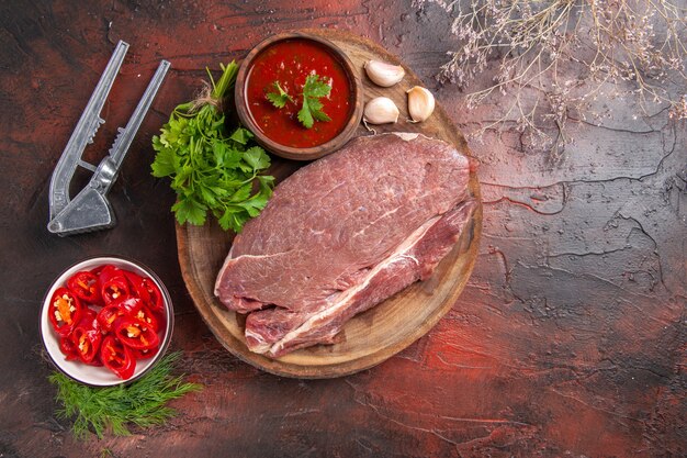 Vista dall'alto di carne rossa su vassoio di legno e ketchup verde all'aglio e pepe tritato su sfondo scuro