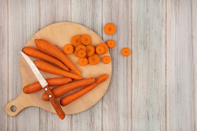 Vista dall'alto di carote alimentari dimagranti su una tavola da cucina in legno con coltello con carote tritate su una parete di legno grigia con spazio di copia