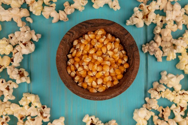 Vista dall'alto di chicchi di popcorn su una ciotola di legno con popcorn isolato su un tavolo di legno blu