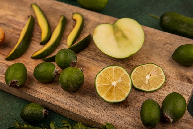 Vista dall'alto di cibi sani come fette di avocado feijoas mezzo lime e mela isolata su una tavola di cucina in legno su uno sfondo verde