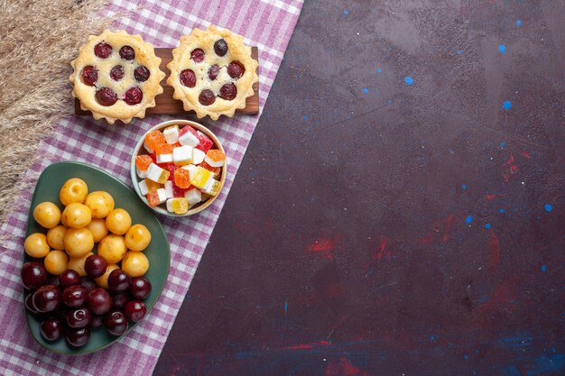 Vista dall'alto di ciliegie dolci fresche all'interno del piatto con torte e caramelle sulla superficie scura