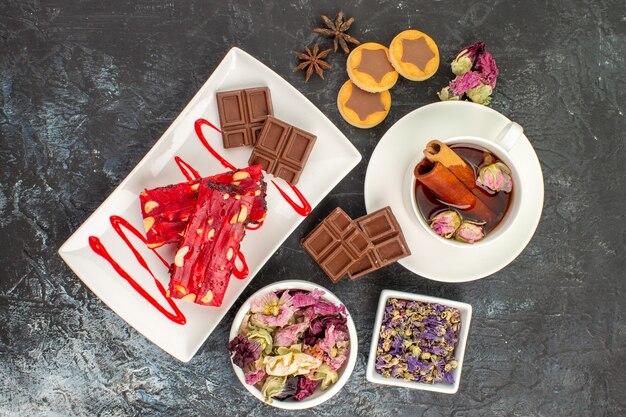 Vista dall'alto di cioccolatini sul piatto bianco con tisane e fiori secchi e biscotti su fondo grigio