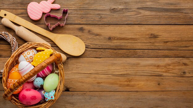 Vista dall'alto di colorate uova di Pasqua nel cesto con utensili da cucina e copia spazio