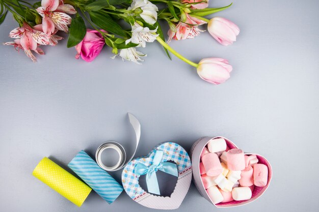 Vista dall'alto di colore rosa e bianco tulipano e fiori di rosa con alstroemeria e scatola regalo a forma di cuore riempito con marshmallow sul tavolo bianco