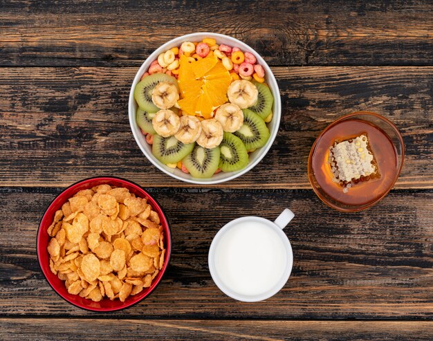 Vista dall'alto di cornflakes con frutta e miele su superficie di legno scuro orizzontale