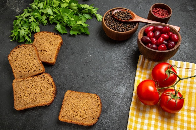 Vista dall'alto di cornioli rossi freschi con verdi pagnotte di pane scuro e pomodori sulla superficie grigia