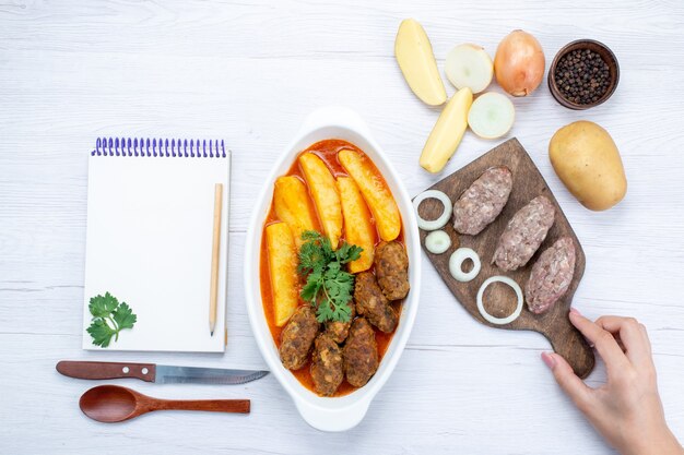 Vista dall'alto di cotolette di carne cotta con salsa di patate e verde insieme a carne cruda sulla scrivania leggera, verdura di carne di farina di cibo