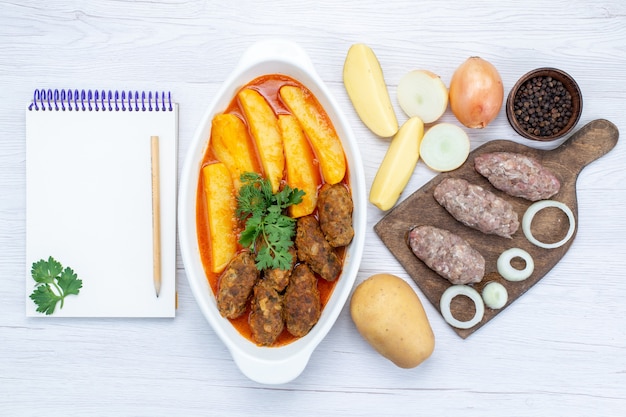 Vista dall'alto di cotolette di carne cotta con salsa di patate e verde insieme a carne cruda sulla scrivania leggera, verdura di carne di farina di cibo