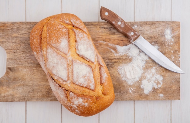 Vista dall'alto di crosta di pane con coltello e farina sul tagliere su fondo in legno