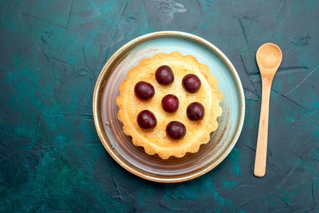 Vista dall'alto di cupcake con amarene accanto al cucchiaio su blu scuro,