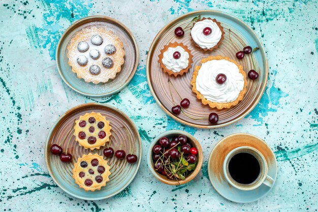 Vista dall'alto di cupcakes con ciliegie, zucchero in polvere e panna accanto all'americano