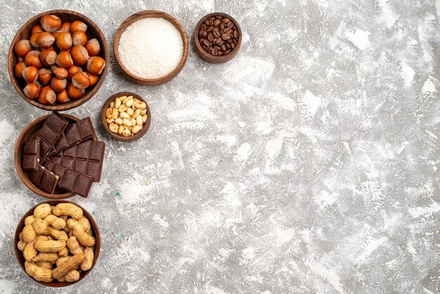 Vista dall'alto di deliziose barrette di cioccolato con nocciole e arachidi sulla superficie bianca