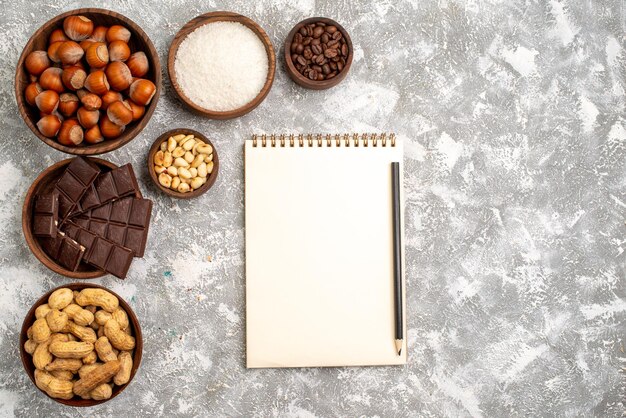 Vista dall'alto di deliziose barrette di cioccolato con nocciole e arachidi sulla superficie bianca