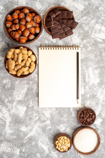 Vista dall'alto di deliziose barrette di cioccolato con nocciole e arachidi sulla superficie bianca