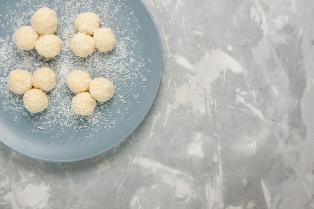 Vista dall'alto di deliziose caramelle al cocco all'interno del piatto blu su superficie bianca