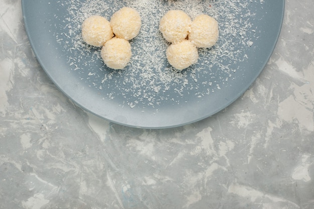 Vista dall'alto di deliziose caramelle al cocco all'interno del piatto blu sulla scrivania bianca