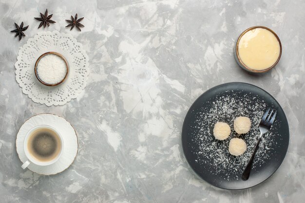 Vista dall'alto di deliziose caramelle al cocco con una tazza di caffè sulla superficie bianca