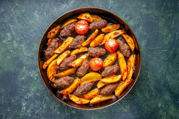 Vista dall'alto di deliziose cotolette di carne al forno con patate e pomodori su sfondo di colore misto verde e nero