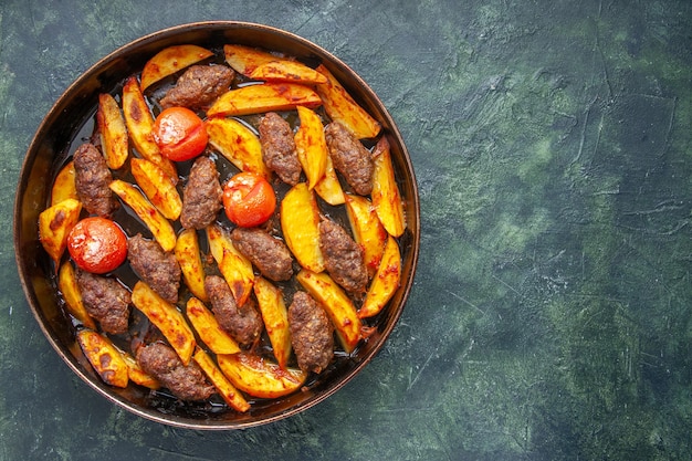 Vista dall'alto di deliziose cotolette di carne al forno con patate e pomodori sul lato destro su sfondo di colore verde e nero misto