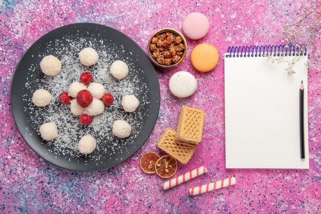 Vista dall'alto di deliziose palline dolci di caramelle al cocco con macarons francesi e cialde sulla scrivania rosa
