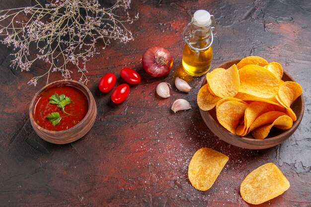 Vista dall'alto di deliziose patatine croccanti fatte in casa all'interno e all'esterno della bottiglia di olio marrone ketchup pomodori aglio cipolla su sfondo scuro