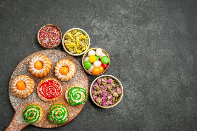 Vista dall'alto di deliziose torte con caramelle e fiori su fondo nero