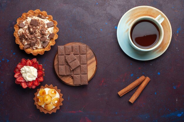 Vista dall'alto di deliziose torte con crema al cioccolato e frutta insieme al tè sulla superficie scura