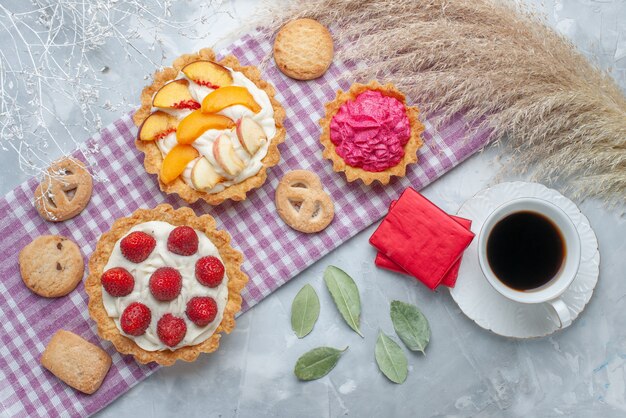 vista dall'alto di deliziose torte cremose con frutta a fette insieme a biscotti e tè sulla scrivania leggera, torta biscotto crema dolce cuocere