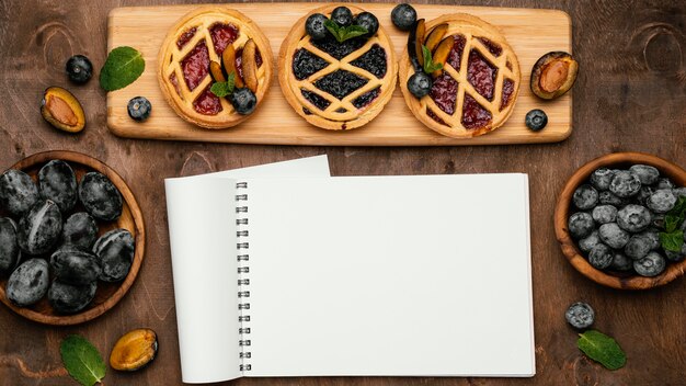 Vista dall'alto di deliziose torte di frutta con prugne e taccuino