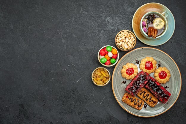 Vista dall'alto di deliziose torte fruttate con biscotti e tazza di tè al buio