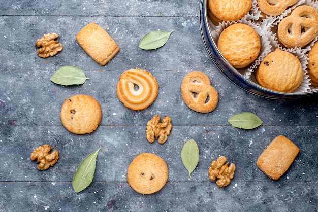 Vista dall'alto di deliziosi biscotti diversi formati all'interno del pacchetto rotondo con noci sulla scrivania grigia, biscotto biscotto torta dolce zucchero