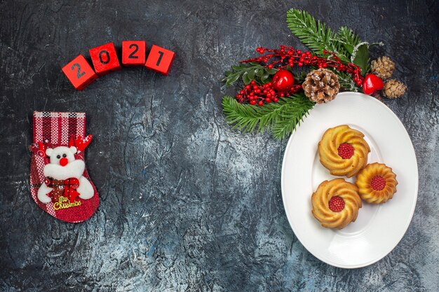 Vista dall'alto di deliziosi biscotti su un piatto bianco e decorazioni cappello di babbo natale numeri calzino di capodanno su superficie scura