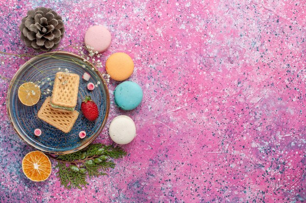 Vista dall'alto di deliziosi macarons francesi con cialde sulla superficie rosa