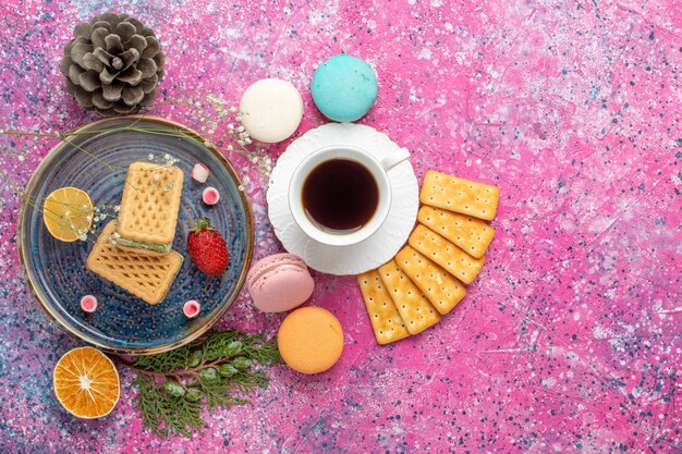 Vista dall'alto di deliziosi waffle con cracker macarons francesi e tè sulla superficie rosa