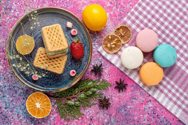 Vista dall'alto di deliziosi waffle con macarons francesi sulla scrivania rosa chiaro